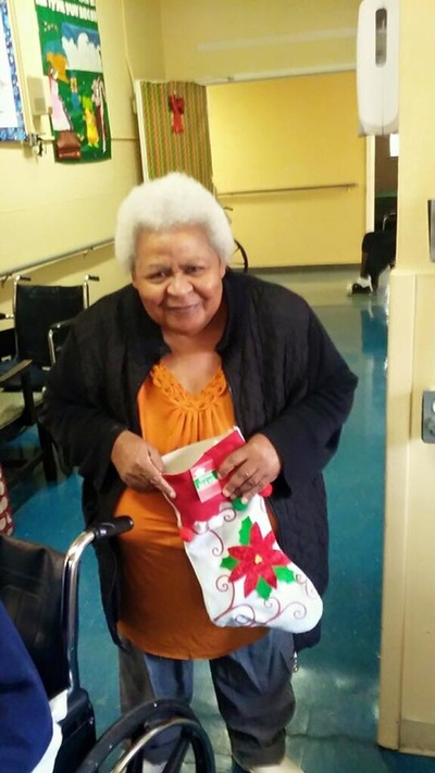 A nursing home resident smiling while holding her Christmas stocking